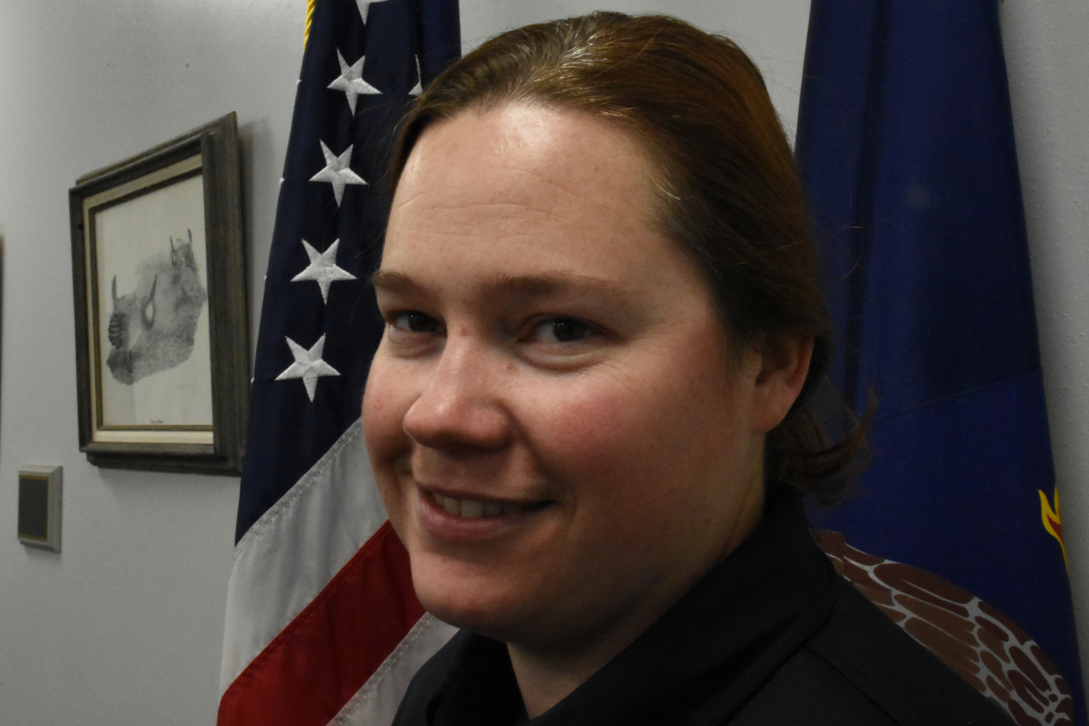 A woman standing and smiling in front of flags.