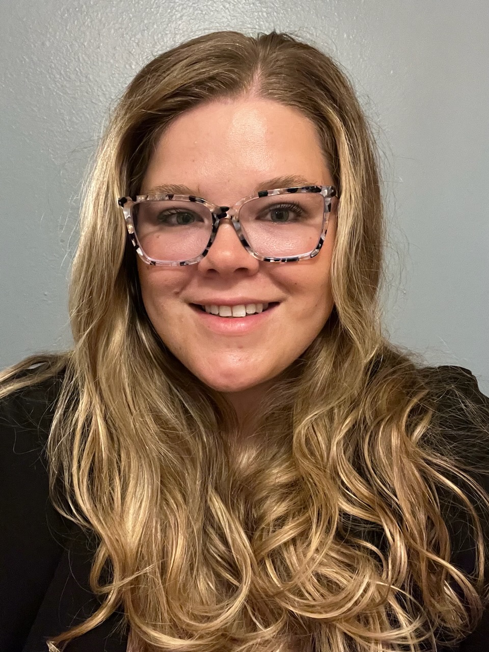 A woman wearing glasses smiling at the camera.